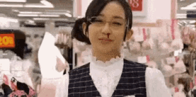 a woman wearing glasses and a vest is standing in front of a store .