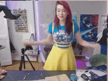 a woman in a yellow skirt and a blue shirt is standing in front of a camera .