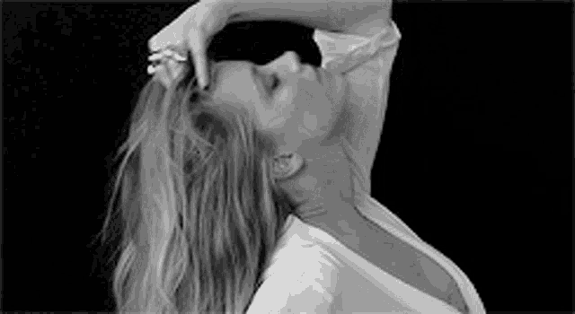 a woman in a white shirt is holding her hair in a black and white photo .