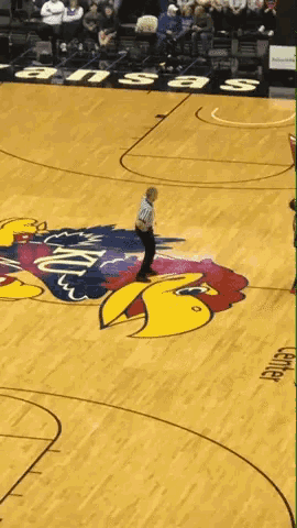 a referee stands on a basketball court in front of a kansas logo