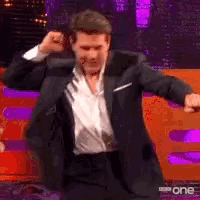 a man in a suit and white shirt is dancing in front of a sign that says bbc one