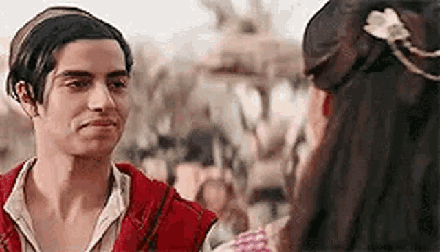 a man and a woman are looking at each other . the man is wearing a red vest .