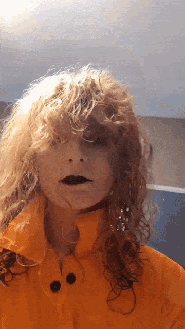 a woman with curly hair is wearing an orange jacket