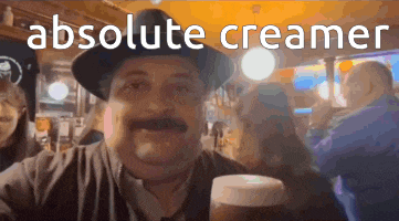 a man in a hat is holding a glass of beer with the words " absolute creamer " behind him