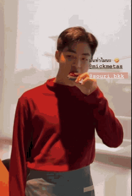 a man in a red sweater is brushing his teeth with a toothbrush
