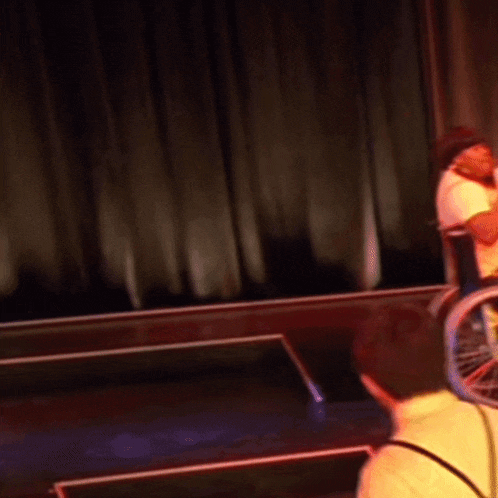 a person in a wheelchair stands on a stage in front of a red curtain