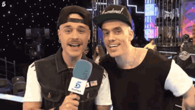 two men are standing next to each other and one of them is holding a microphone that says 5 on it