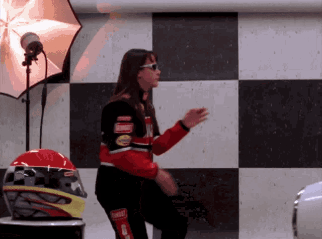 a woman wearing a simpson racing suit is dancing in front of a checkered wall