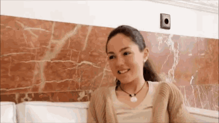 a young woman is smiling while sitting on a couch in front of a red marble wall .