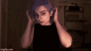 a girl with purple hair is wearing a black shirt and holding her hair .
