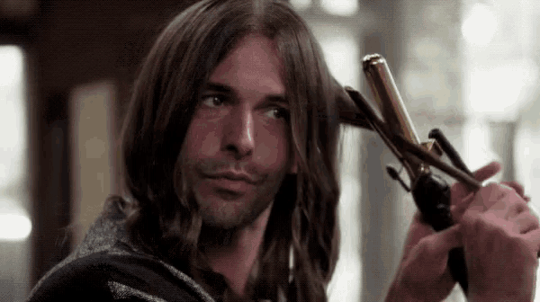a man with long hair is holding a gold curling iron