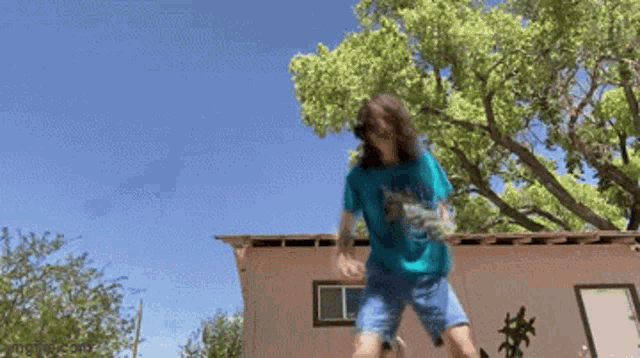 a man in a blue shirt is jumping in front of a building