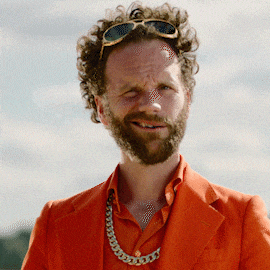 a man with curly hair and a beard wearing sunglasses and an orange jacket