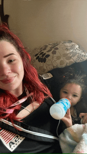 a woman with red hair is holding a baby with a bottle and a lanyard that says nfl on it