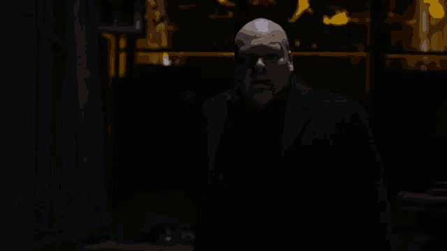 a bald man in a suit is standing in a dark room