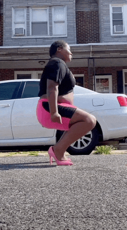 a woman wearing pink high heels squats in front of a white car
