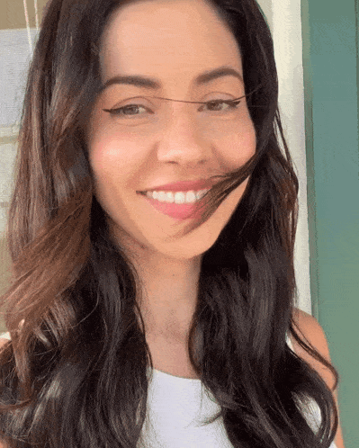 a woman with long dark hair is smiling with her hair blowing in her face