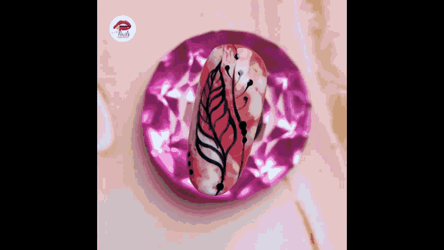 a nail with a feather design on it is sitting on a pink plate .