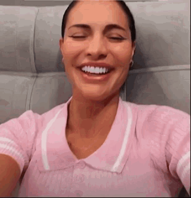 a woman in a pink shirt is smiling and taking a selfie with her eyes closed .