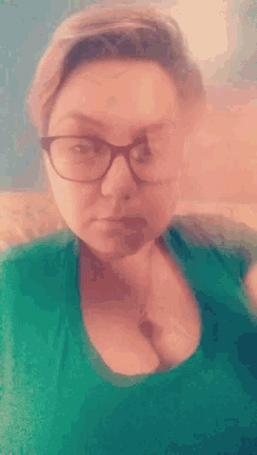 a woman wearing glasses and a green shirt is making a face