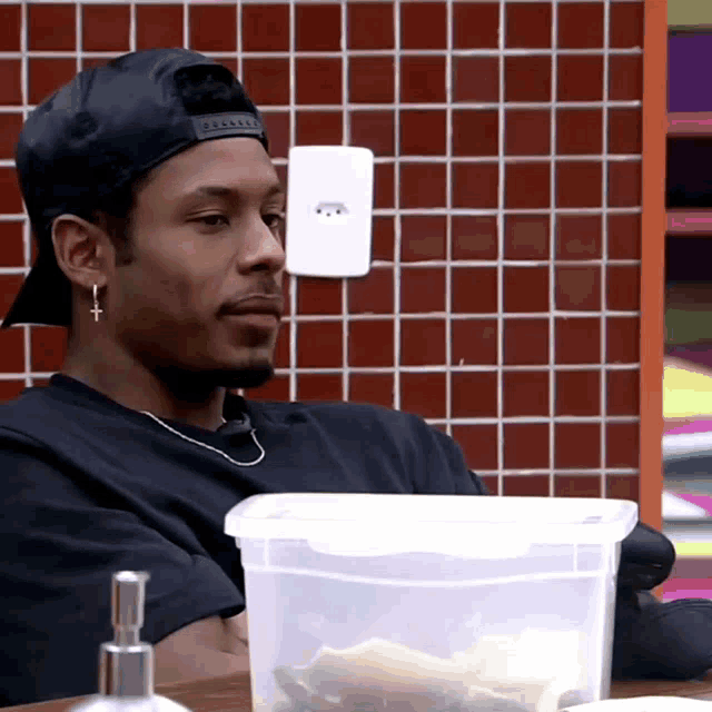 a man wearing a black hat sits at a table with a plastic container in front of him