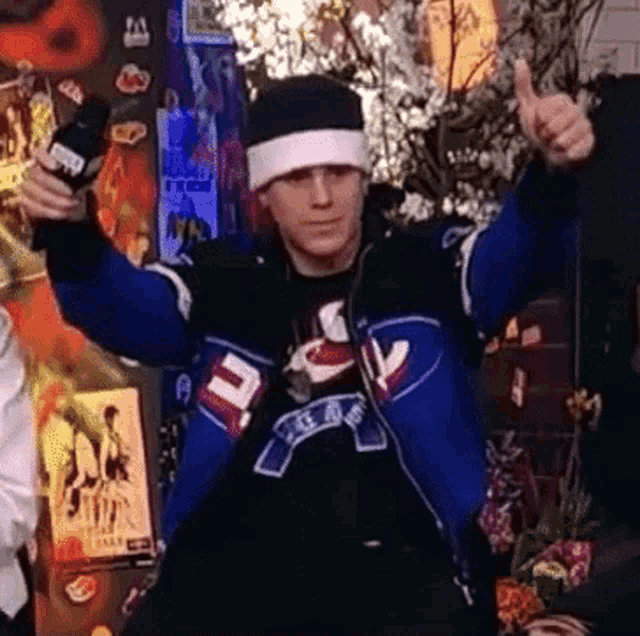 a man giving a thumbs up while wearing a blue jacket with the letter t on it