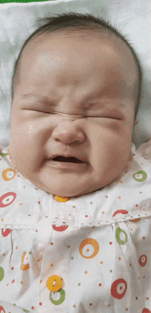 a baby in a polka dot dress is crying with its eyes closed
