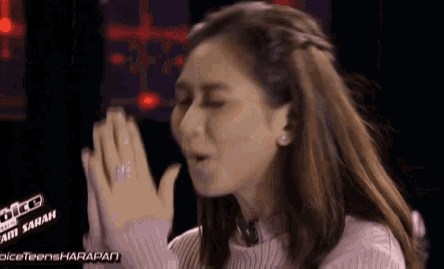 a woman in a pink sweater is making a funny face with her hands together .