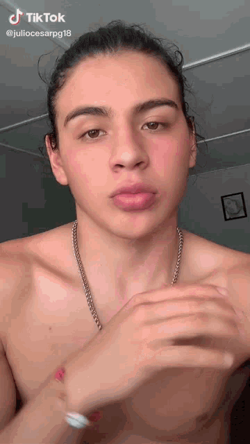 a young man without a shirt is wearing a chain around his neck and a bracelet on his wrist ..