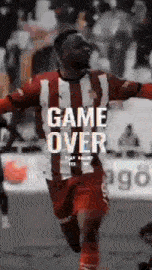 a man in a red and white striped shirt is running on a soccer field with the words game over above him .
