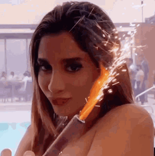 a naked woman is holding a candle with sparks coming out of it in front of a pool .