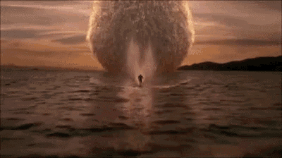 a person is riding a jet ski in the water with a large explosion in the background .