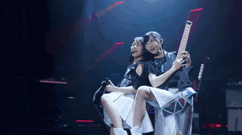 a girl holding a guitar while another girl looks on