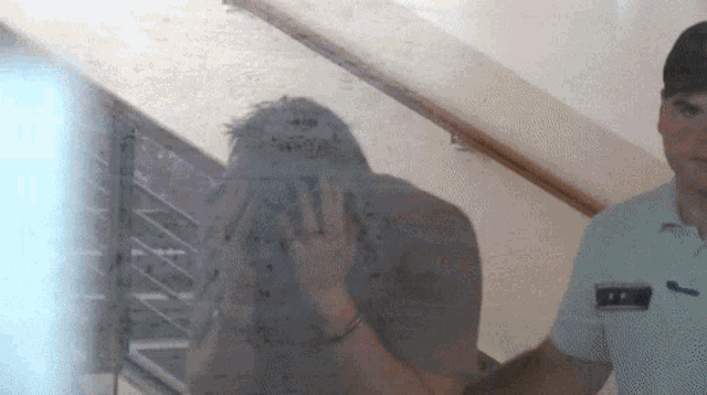 a man covering his face is being escorted by a police officer with a badge that says ' a. '