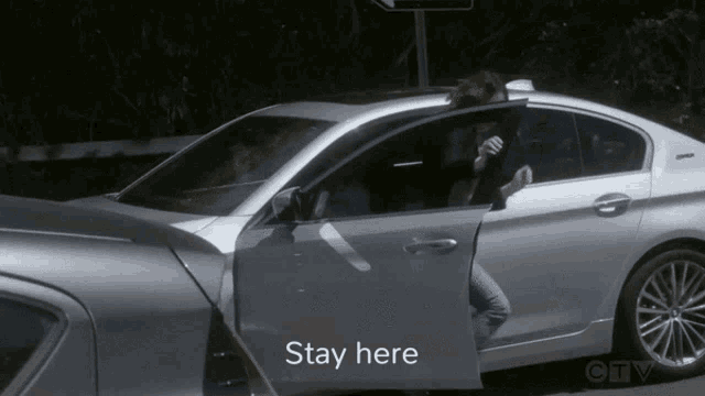 a woman is getting out of a silver car with the words stay here on the bottom