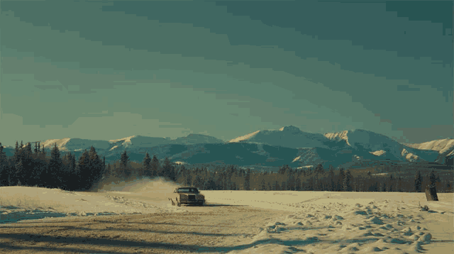 a car is driving down a snowy road in the mountains