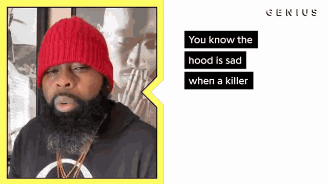 a man with a beard wearing a red beanie and a black hoodie with genius written on the bottom
