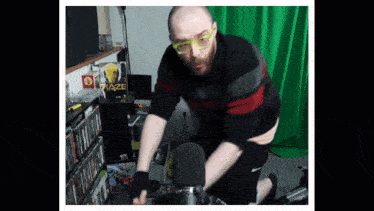a man wearing glasses is kneeling in front of a green screen with maze written on it