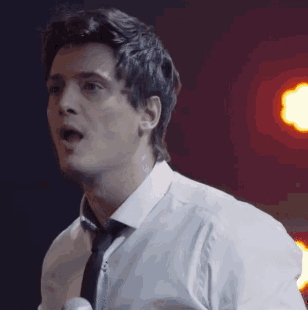 a man in a white shirt and black tie is singing into a microphone
