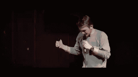 a man is standing in front of a microphone on a stage and singing into it .