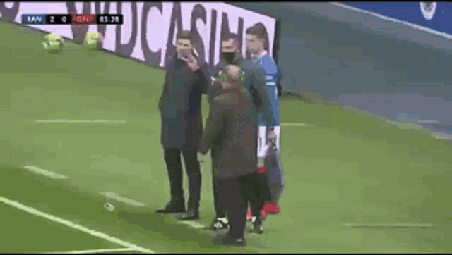 a group of men are standing on a soccer field with a score of 2 to 1