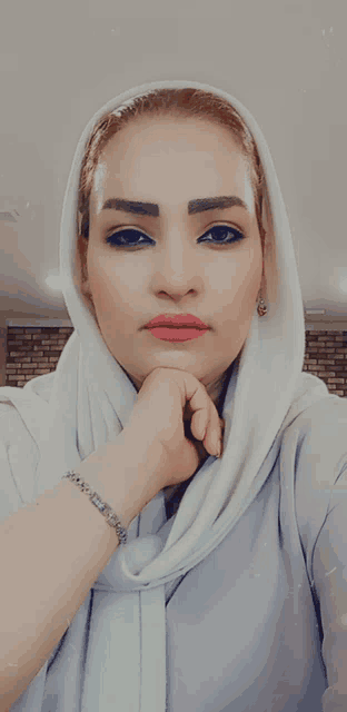 a woman wearing a white scarf and a silver bracelet takes a selfie