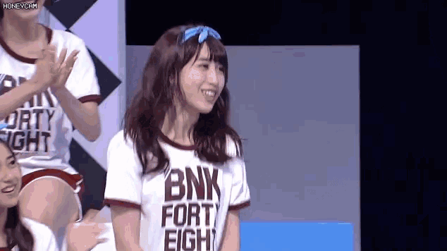 a woman wearing a bnk fort eight shirt is smiling