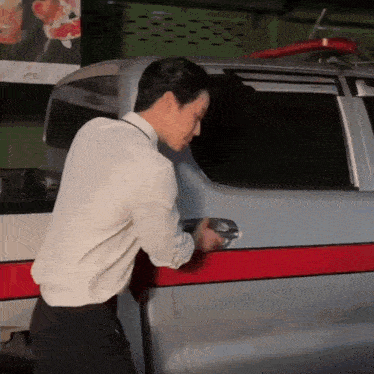 a man in a white shirt and black pants opens the door of a silver van