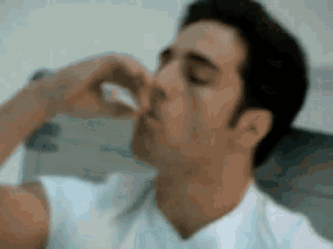 a man in a white shirt is blowing his nose with a tissue