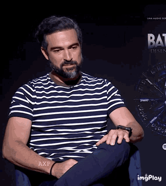 a man in a striped shirt sits in front of a sign that says bat