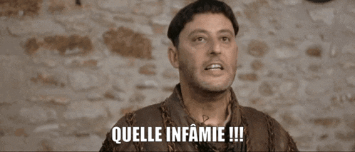 a man with a shaved head says " quelle infamie " in front of a stone wall