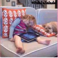 a little girl is laying on a couch playing with a tablet