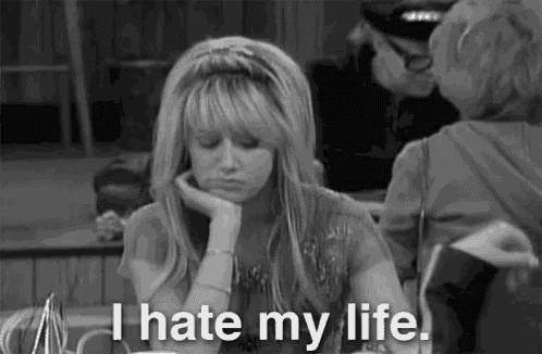 a black and white photo of a woman sitting at a table with her hand on her chin and the words `` i hate my life '' .