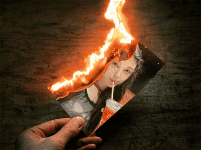 a person is holding a burning photo of a girl drinking a coke through a straw